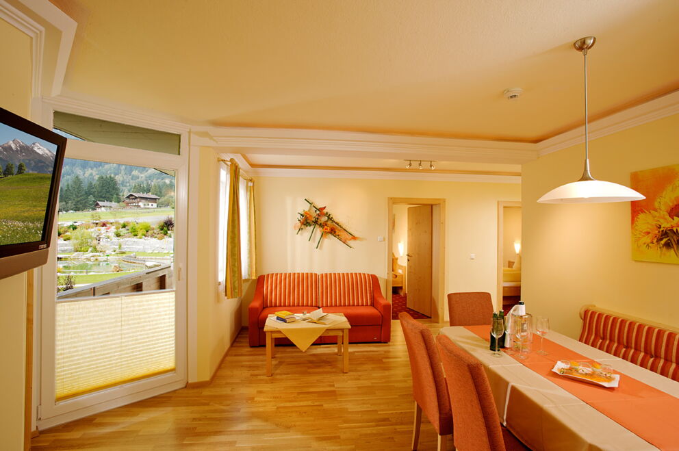 Gemütliches Zimmer mit Holzboden, großem Fenster, Sitzbereich und Esstisch.
