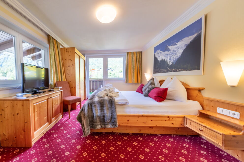 Einladendes Zimmer mit Holzmöbeln und Balkonblick auf die Alpenlandschaft.