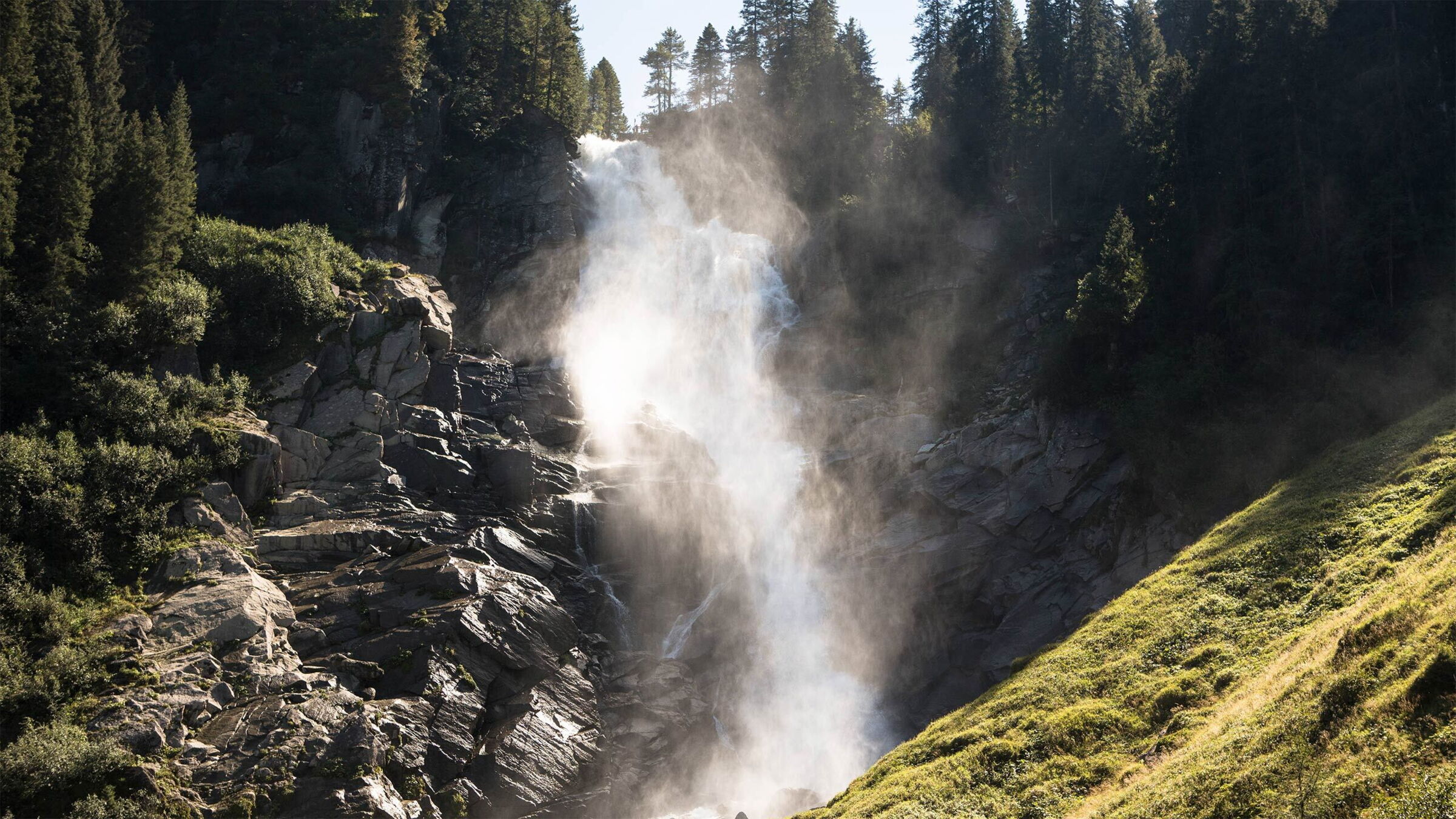 Ein beeindruckender Wasserfall fließt über Felsen, umgeben von üppigem Grün und hohen Bäumen.