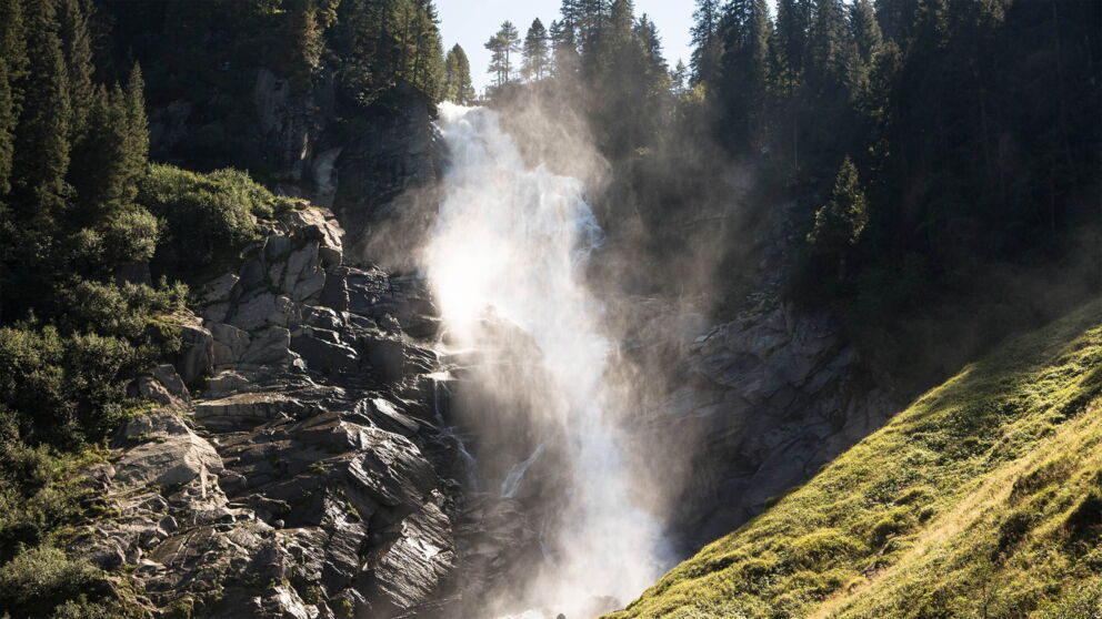 Powerful waterfall in the sunlight, surrounded by dense, green forests.