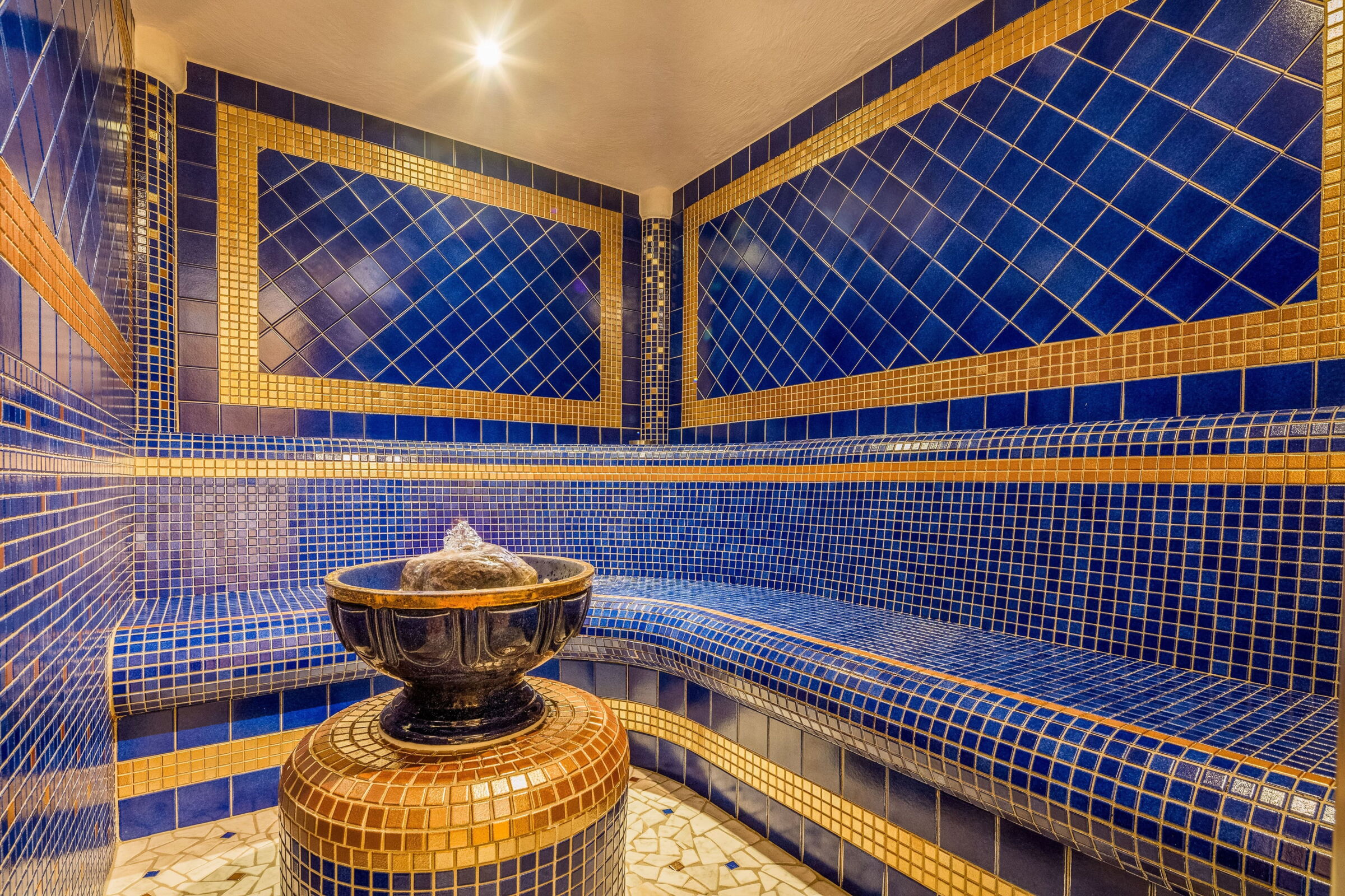 Luxuriöses Dampfbad aus blauen Kacheln mit zentralem Springbrunnen.