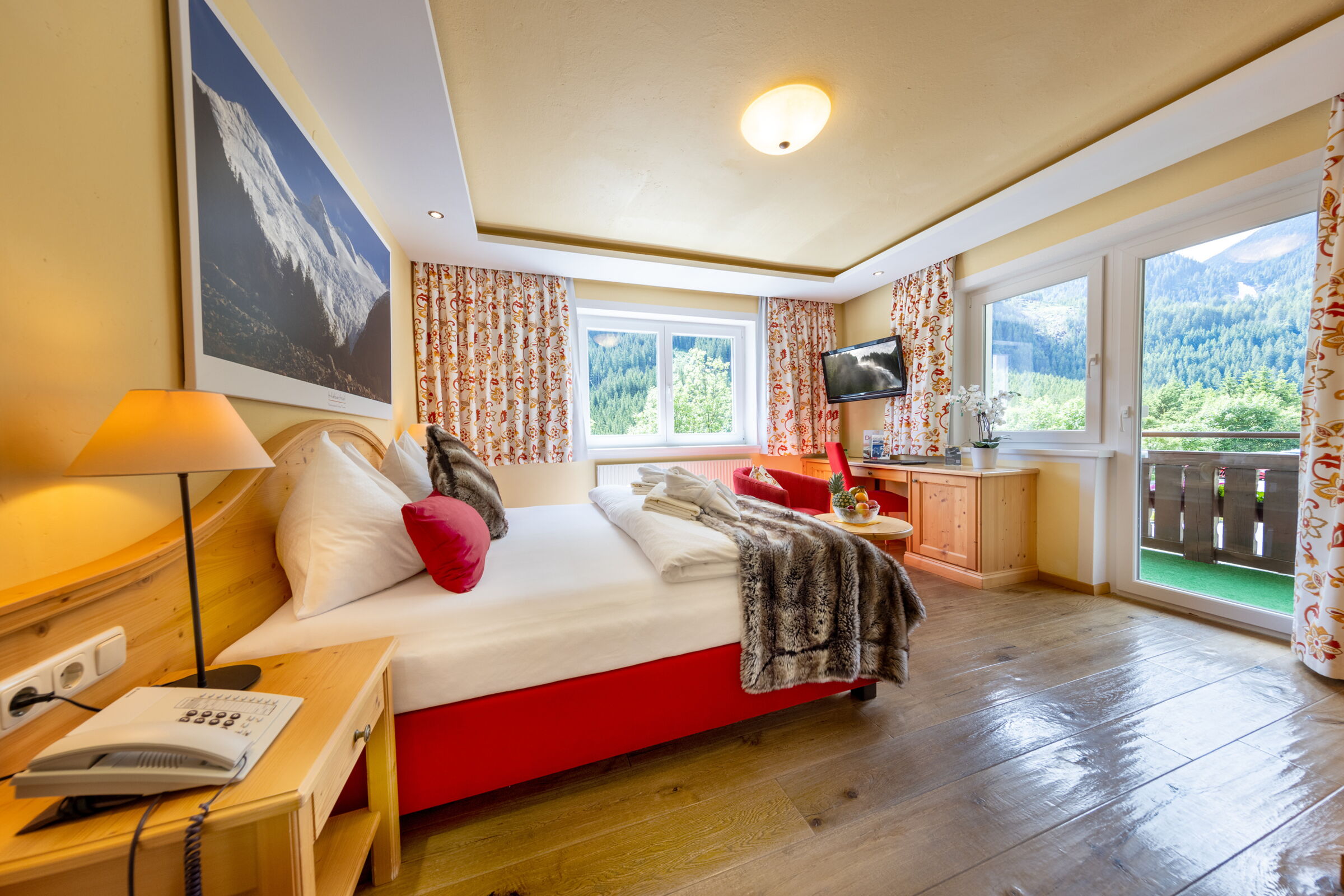 Gemütliches Zimmer mit Bergblick, Holzmöbeln, großen Fenstern und warmem Licht.