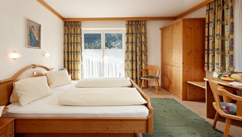 Helles Zimmer mit Holzmöbeln, Doppelbett, Tisch und Blick auf bewaldete Berge.
