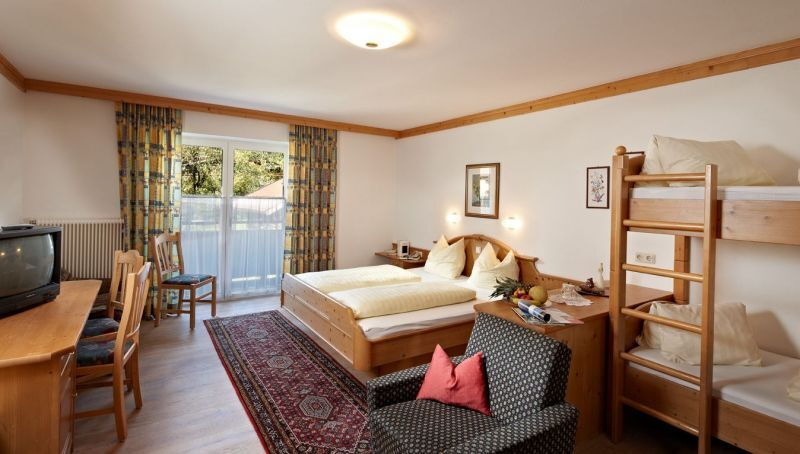 Geräumiges Zimmer mit Doppelbett, Etagenbett, Sessel und Balkon mit Tageslicht.