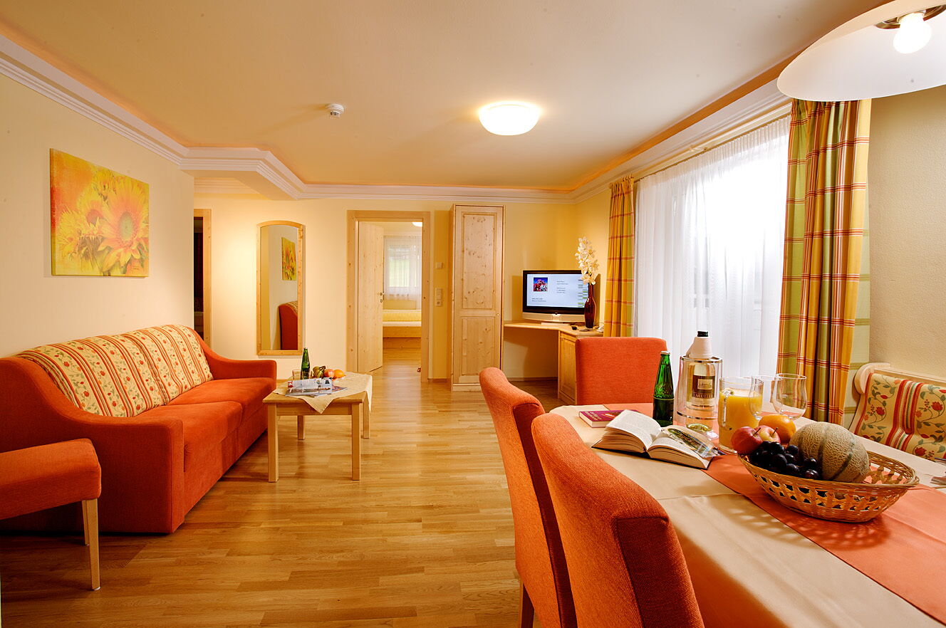 Bright, cozy suite with orange furniture, dining table and TV in the hotel room.