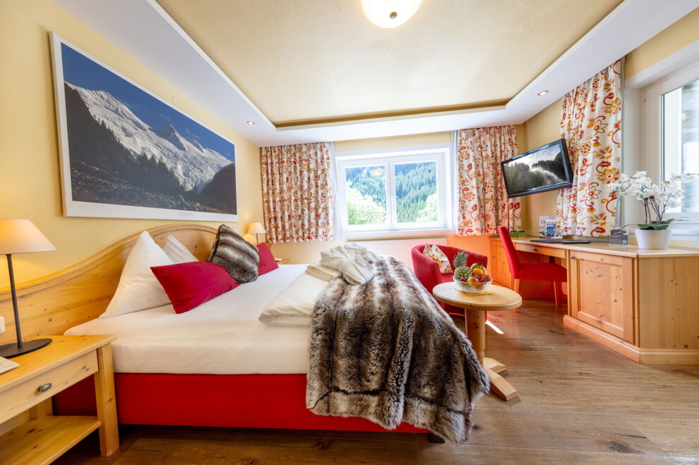 Helles Zimmer mit gemütlichem Bett, warmen Farben und malerischem Bergblick.
