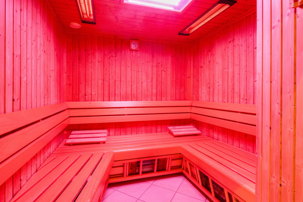 Holzvertäfelte Sauna mit sanfter Infrarotbeleuchtung für entspannende Wärmetherapie.