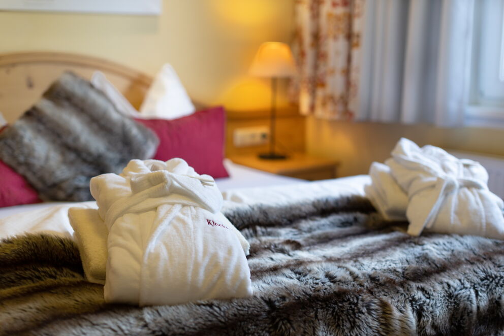 Flauschige Bademäntel auf gemütlichem Bett mit warmem Licht und Fellakzenten.
