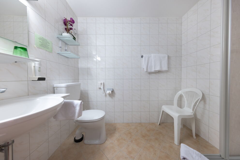 Weiß gefliestes Badezimmer mit Orchidee, Handtüchern und Stuhl für Entspannung.