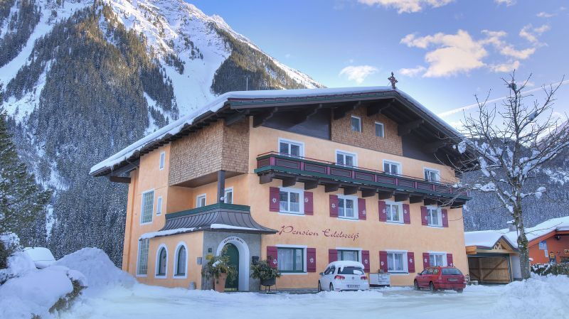 Charmantes Hotel vor verschneiten Bergen, mit blauen Himmel und winterlicher Atmosphäre.