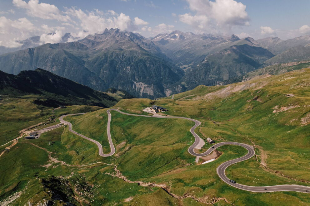 Winding road in the mountains with a majestic backdrop and green meadows.