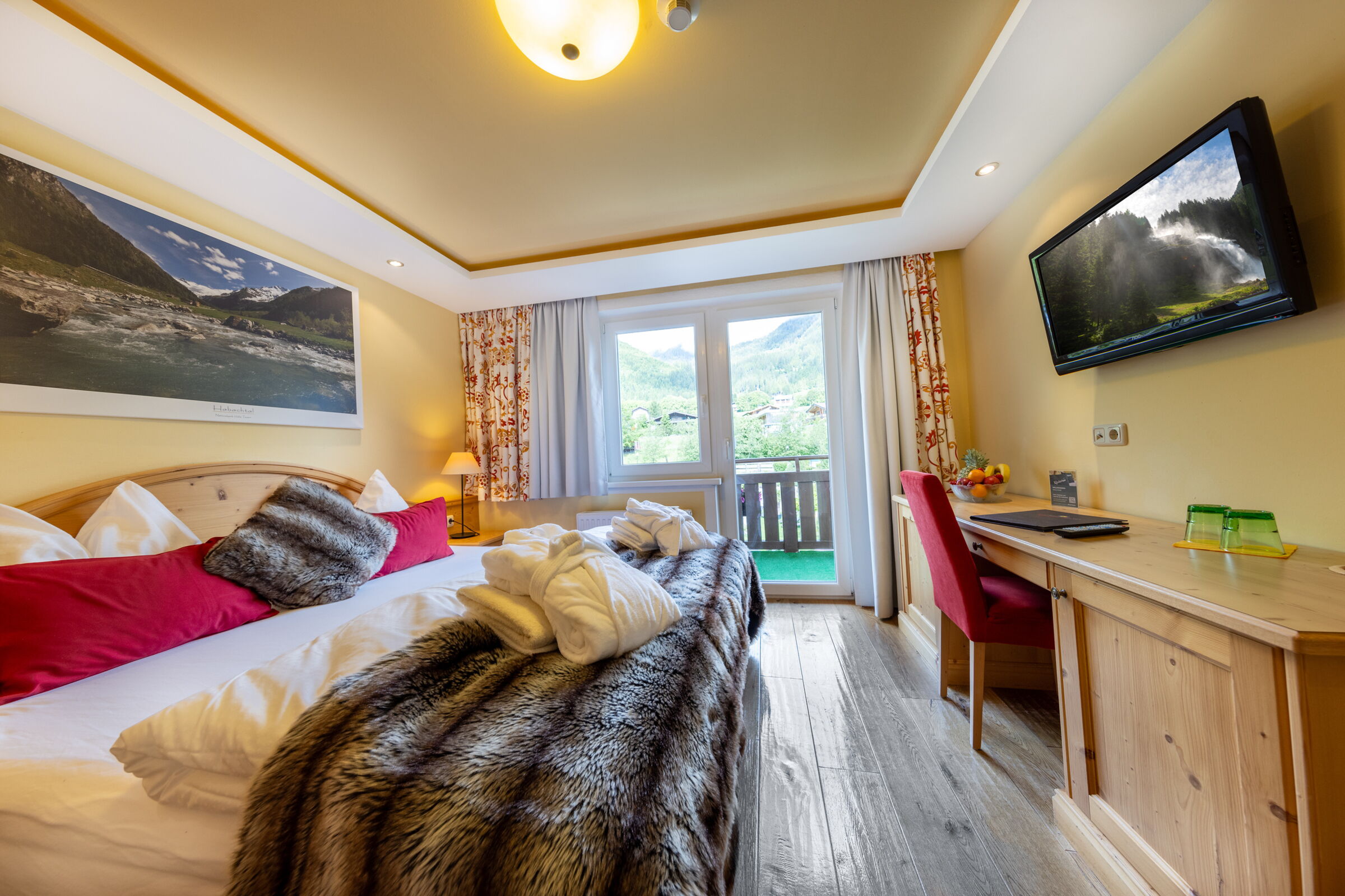 Bright room with wooden floor, large bed and balcony with mountain view.