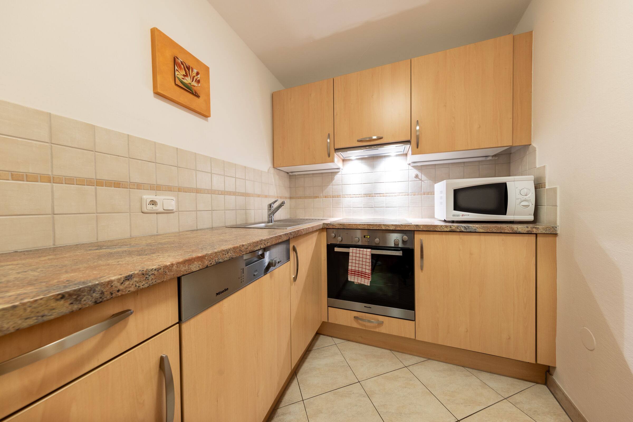 Kleine Küche mit Holzschränken, Spüle, Herd, Mikrowelle und gefliester Rückwand.