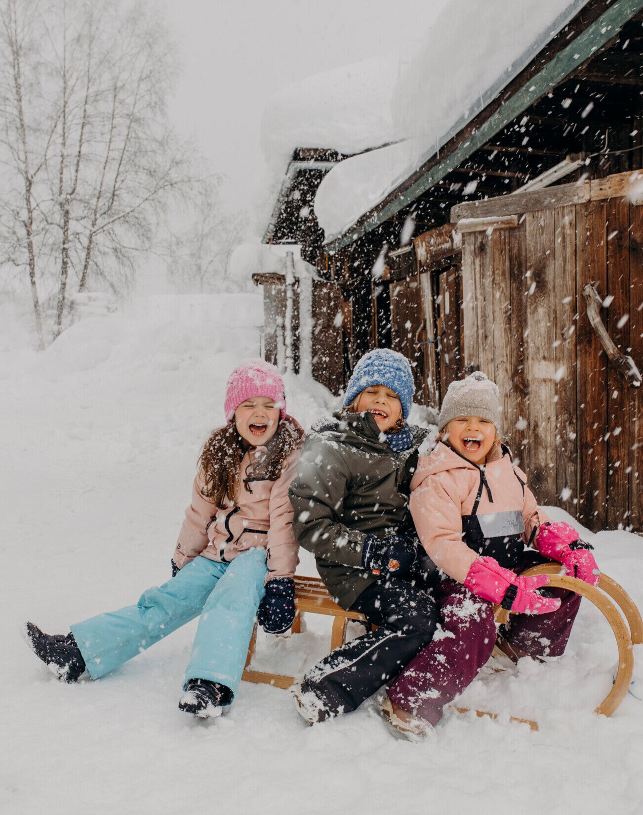 Drei lachende Kinder auf einem Schlitten im verschneiten Winterwunderland.
