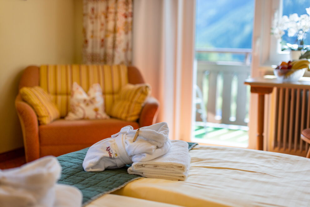 Zimmer mit weichen Handtüchern, Sessel, Balkonblick, hellen Vorhängen und bequemen Betten.