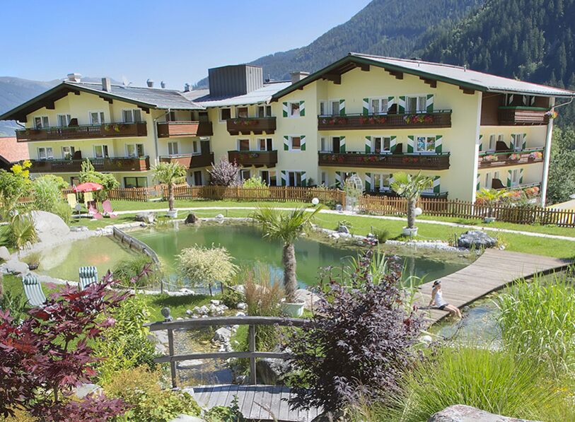 Hotel mit Bio-Schwimmteich und Bergblick, umgeben von üppigem Grün und Blumen.