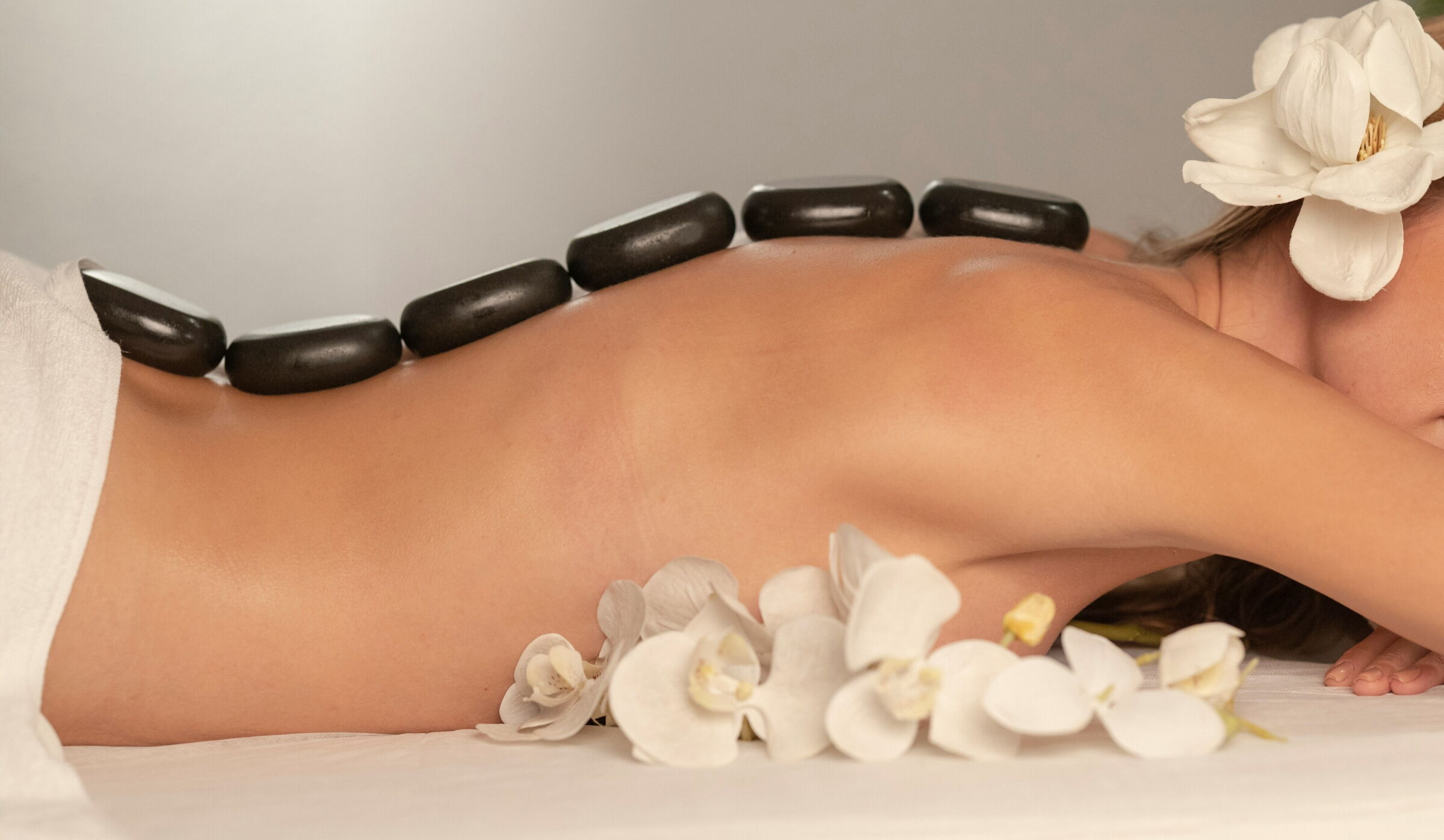 Woman enjoying a hot stone massage with orchid blossoms in the background.