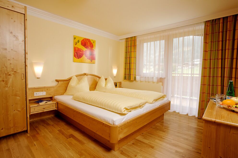 Helles Hotelzimmer mit Doppelbett, Holzinterieur und großem Fenster mit Vorhängen.