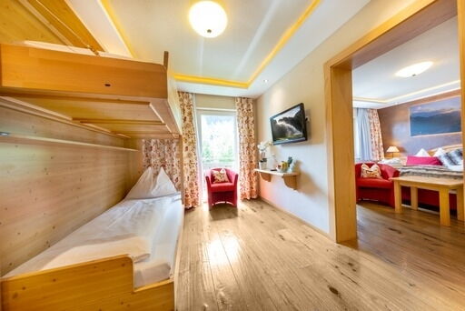 Helles Zimmer mit Holzmöbeln, gemütlicher Sitzecke und großen Fenstern mit Ausblick.