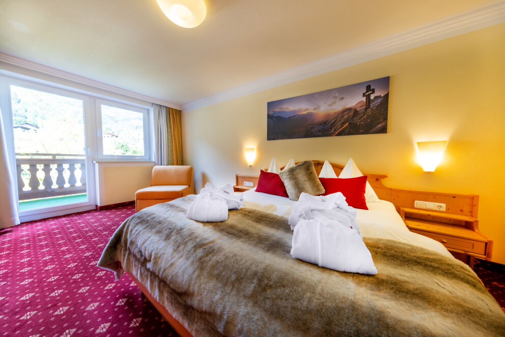 Gemütliches Hotelzimmer mit Balkon, großen Fenstern und dekorativen Kissen auf dem Bett.