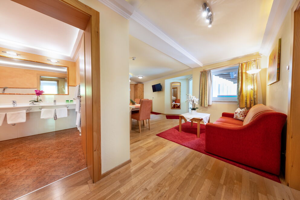 Helles Zimmer mit rotem Sofa, Holzmöbeln und angrenzendem Badezimmer.