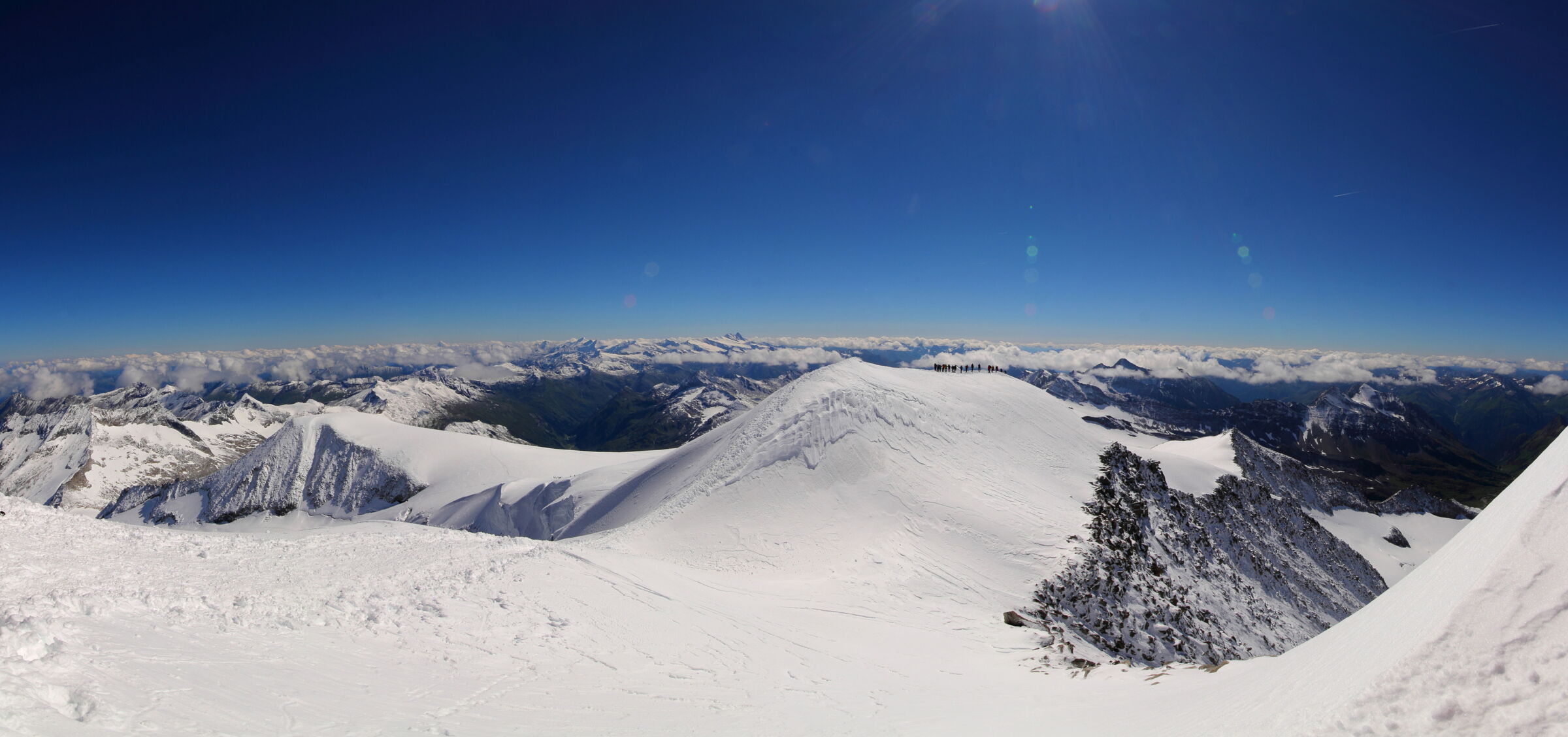 Snow-covered mountain peaks under a clear, bright blue sky in the Alps.