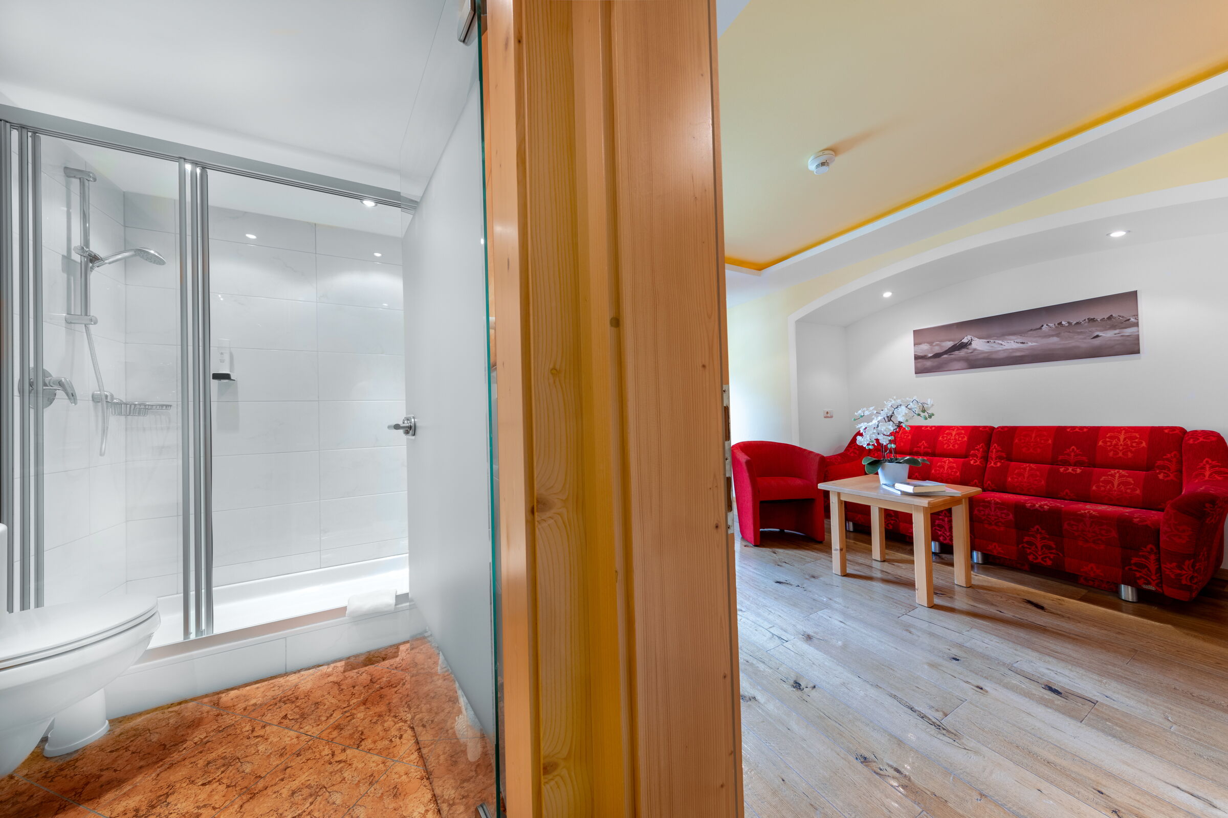 Stilvolles Wohnzimmer mit rotem Sofa und luxuriösem Bad im Hotel Klockerhaus.