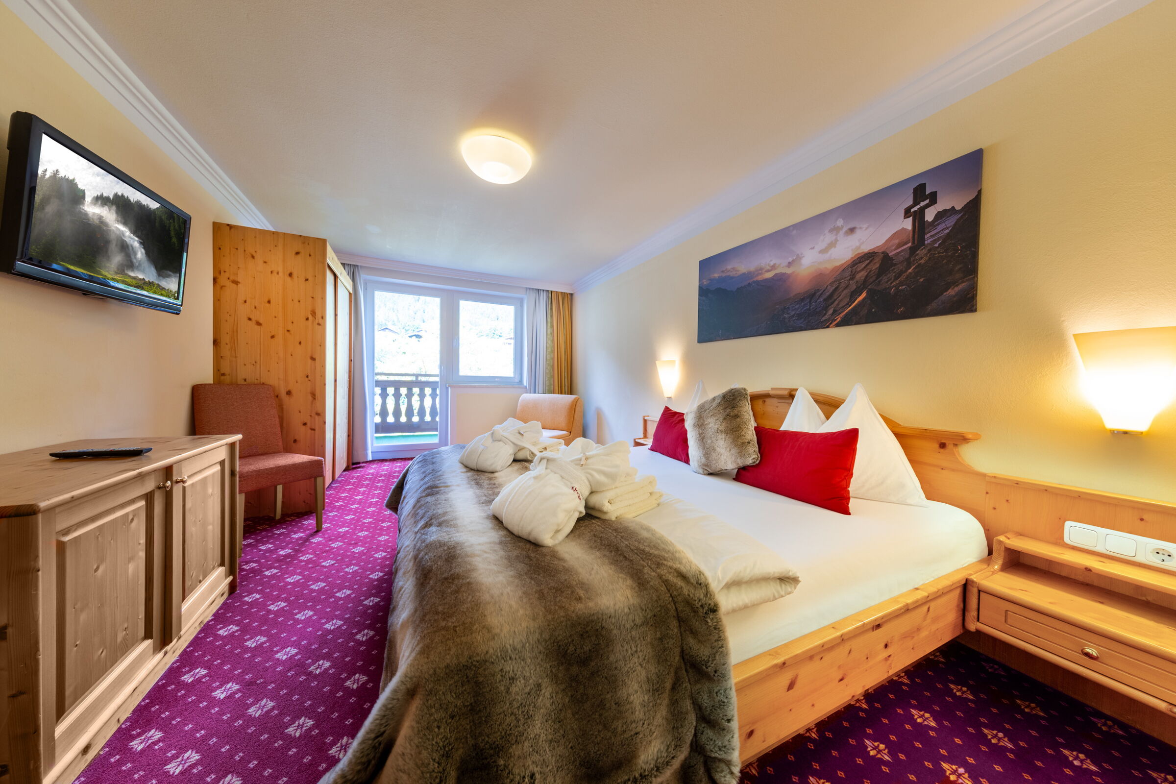 Komfortables Hotelzimmer mit Holzdekor, rotem Teppich und großem Bett in Krimml.