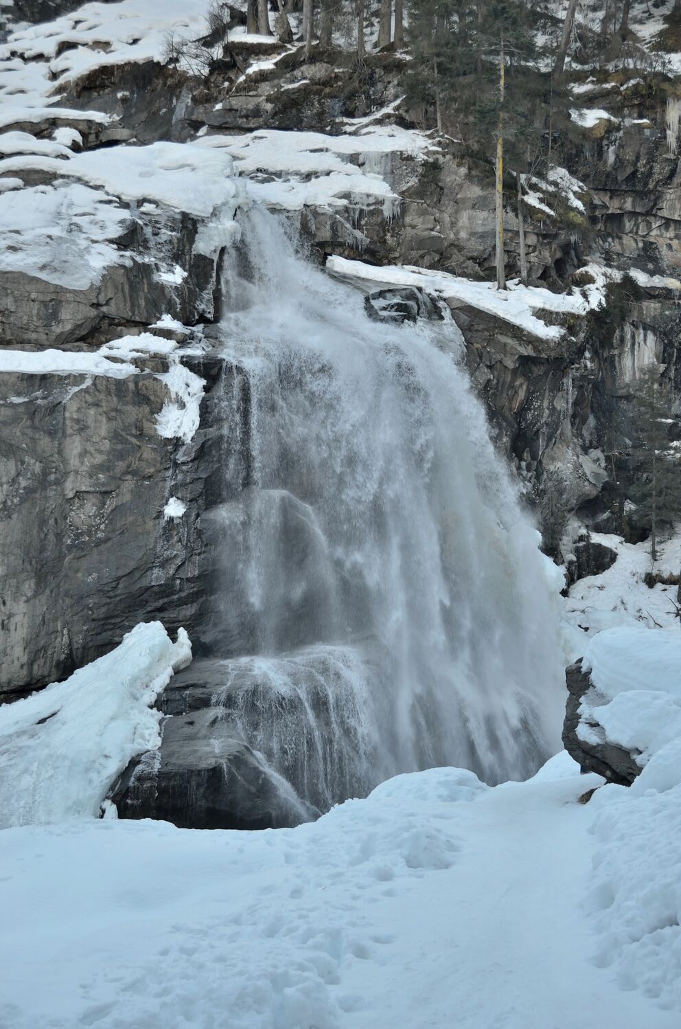 Gefrorener Krimmler Wasserfall umgeben von verschneiten Felsen und winterlicher Landschaft.