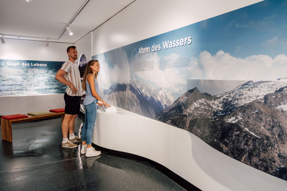 Zwei Personen betrachten eine informative Wand über Wasser und Berge im Hotel.