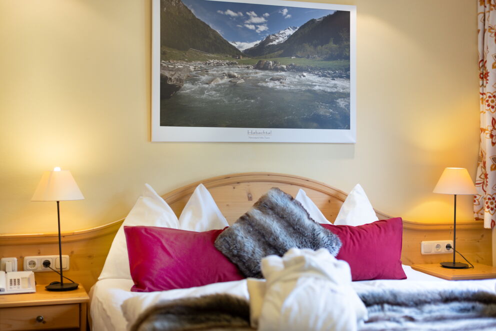 Doppelbett mit kuscheligen Kissen und Naturfoto an der Wand.
