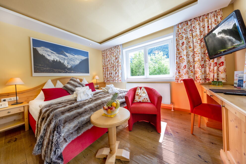 Gemütliches Hotelzimmer mit Alpenblick, rotem Sessel und dekorativen Vorhängen.