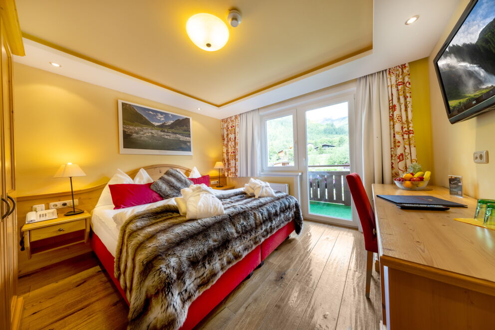 Helles Zimmer mit Holzmöbeln, weicher Bettdecke und Balkonblick auf die Natur.
