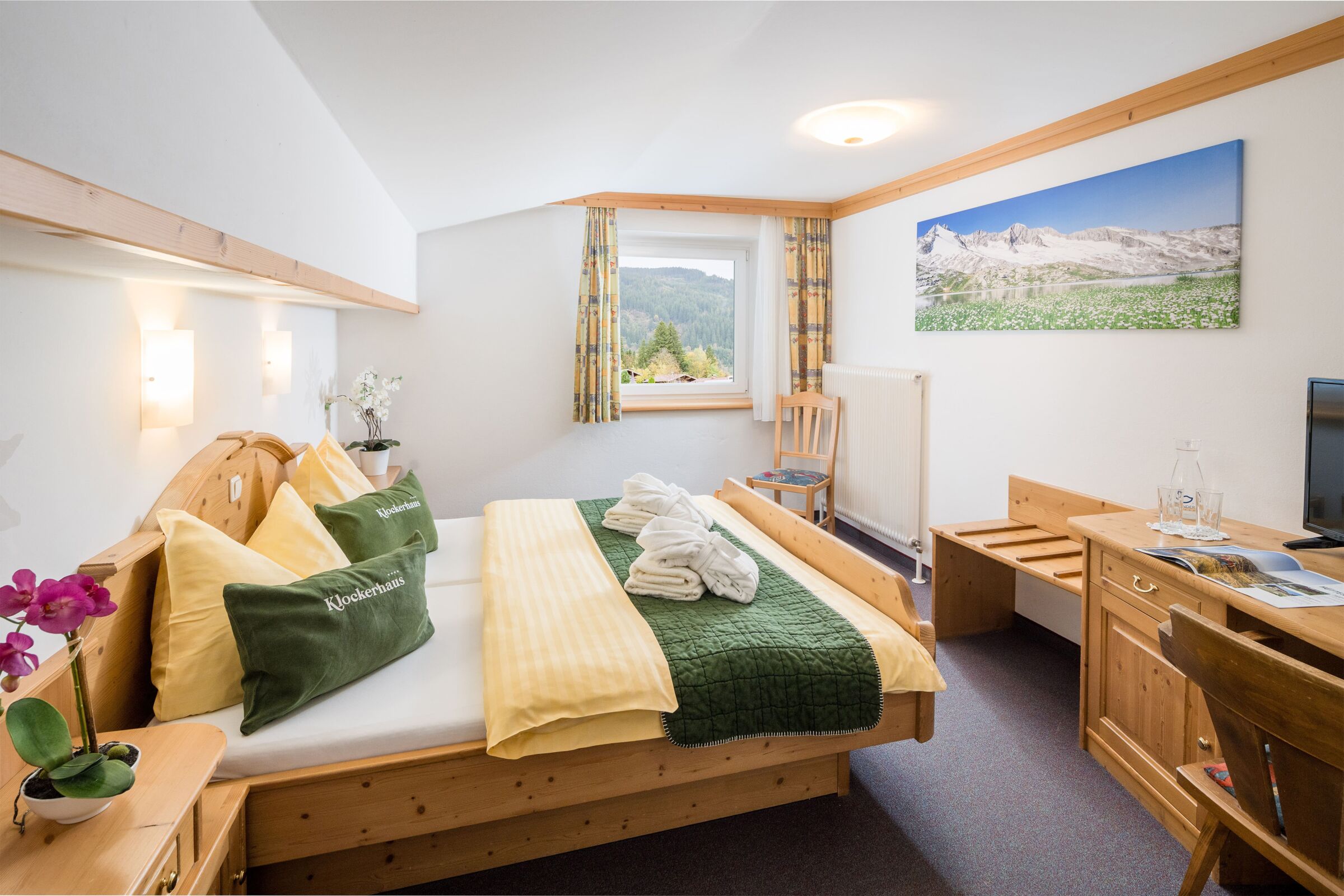 Helles Zimmer mit Holzmöbeln, Bergblick und frischen Blumen auf dem Tisch.
