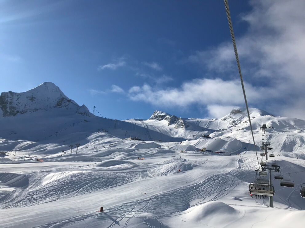 Verschneite Berglandschaft mit Skilift unter strahlend blauem Himmel und majestätischen Gipfeln.