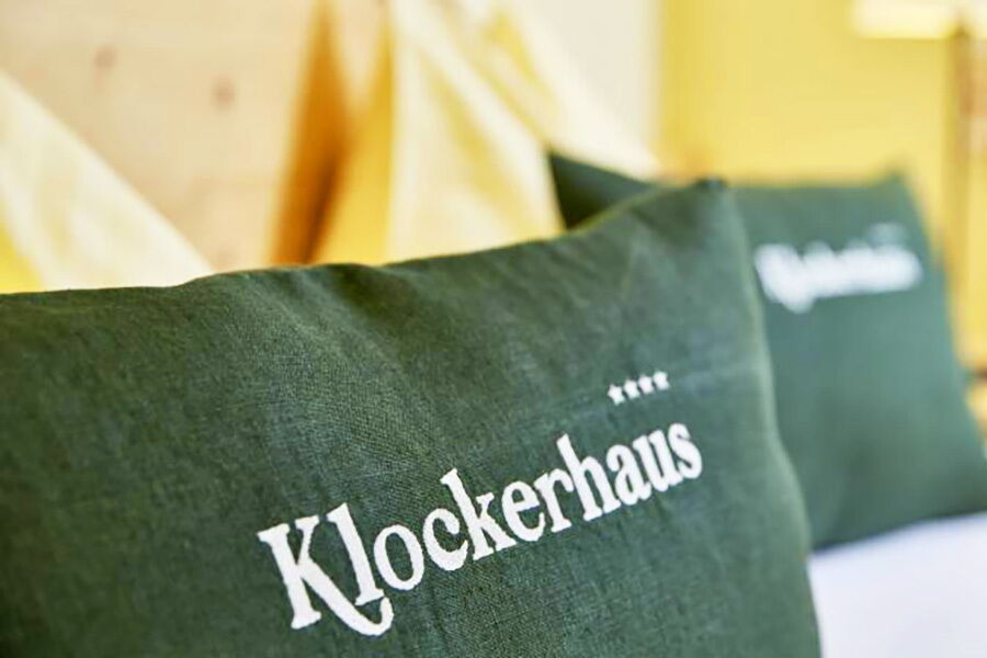 Zwei grüne Kissen mit Klockerhaus-Logo auf einem Bett in einem Hotelzimmer.