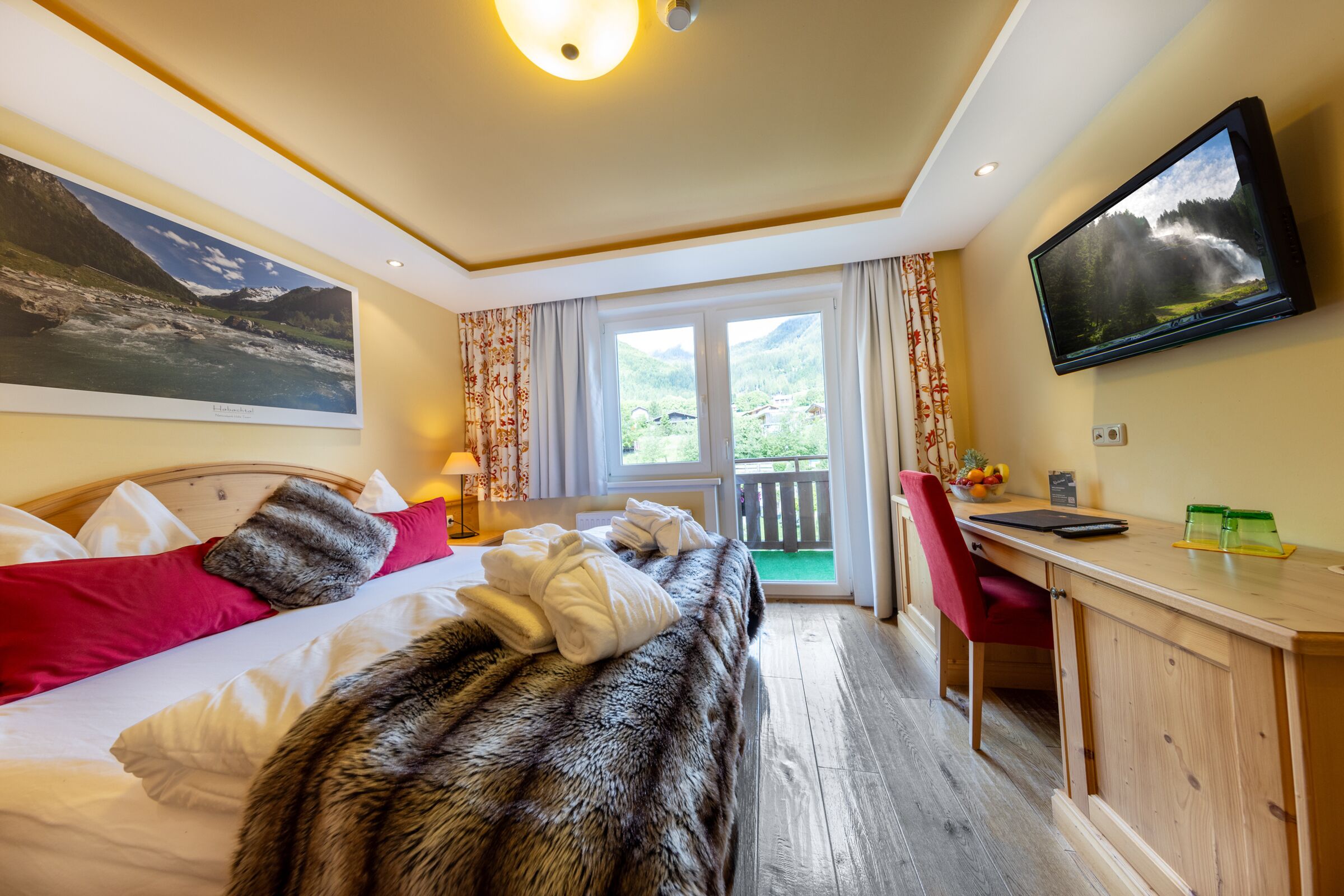 Helles Zimmer mit Holzboden, großem Bett und Balkon mit Bergblick.