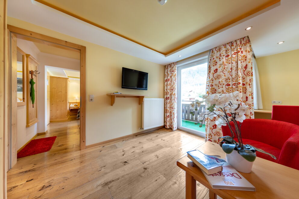 Helles Hotelzimmer mit Holzboden, Balkonzugang und gemütlicher Einrichtung in warmen Farben.