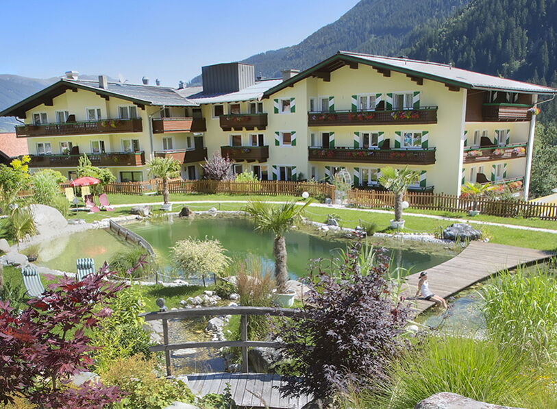 Hotel mit Bio-Schwimmteich und Bergblick, umgeben von üppigem Grün und Blumen.