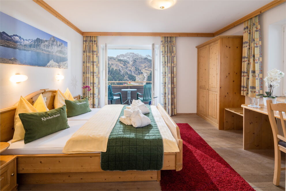 Helles Hotelzimmer mit Holzmöbeln, Balkon und malerischem Bergblick in Krimml.