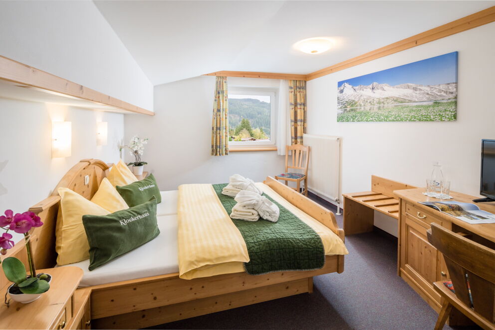 Helles Zimmer mit Holzmöbeln, Bergblick und frischen Blumen auf dem Tisch.