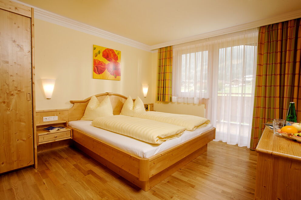 Helles Hotelzimmer mit Doppelbett, Holzinterieur und großem Fenster mit Vorhängen.