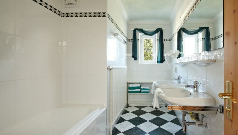 Helles Badezimmer mit Badewanne, zwei Waschbecken und stilvollen Fliesen in Schwarz-Weiß.