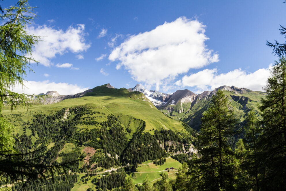 Grüne Täler und beeindruckende Berge unter blauem Himmel mit weißen Wolken.
