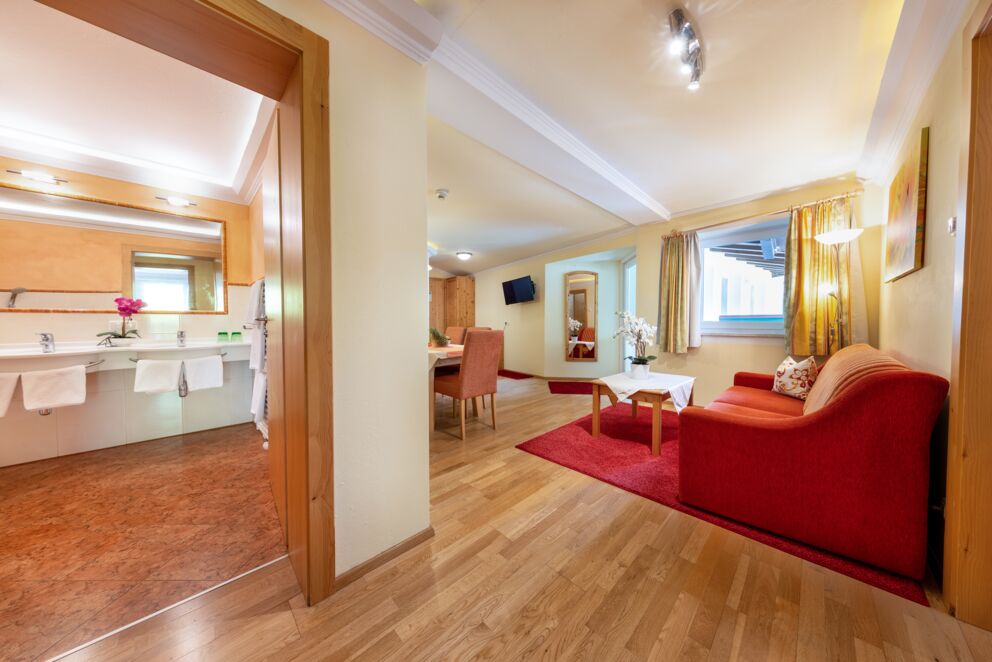 Helles Zimmer mit rotem Sofa, Holzmöbeln und angrenzendem Badezimmer.