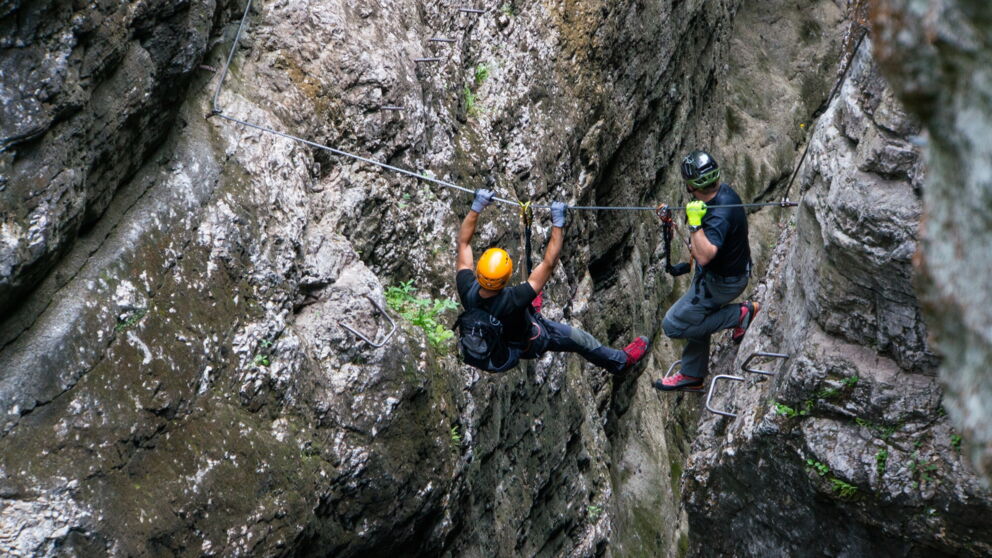 Zwei Kletterer am Seil in einer felsigen Schlucht, Helm und Sicherheitsausrüstung tragend.