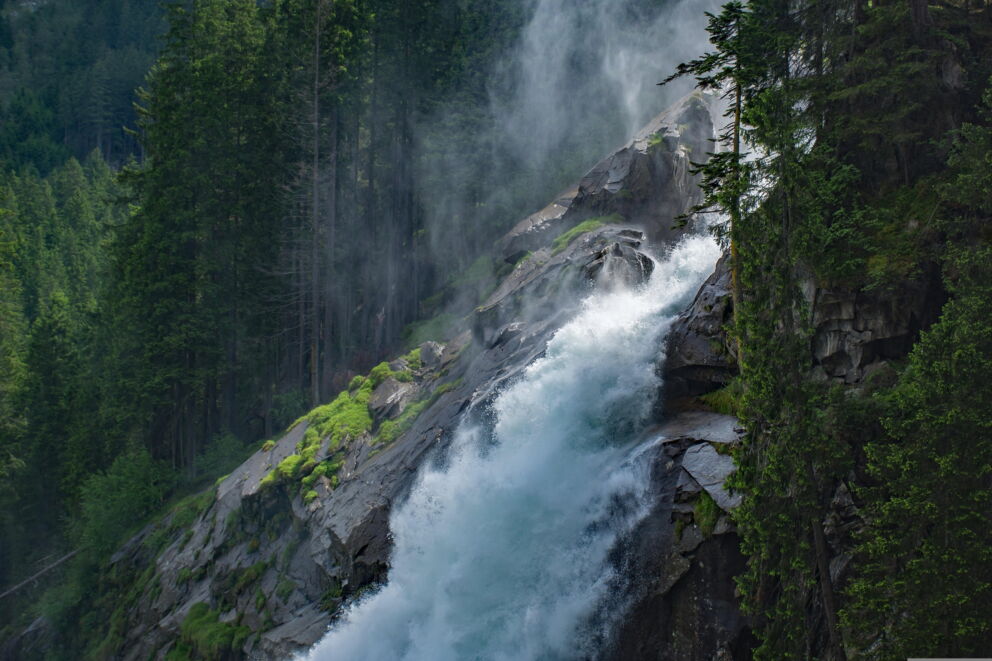 Roaring waterfall in the midst of lush green forests and rocky landscapes.
