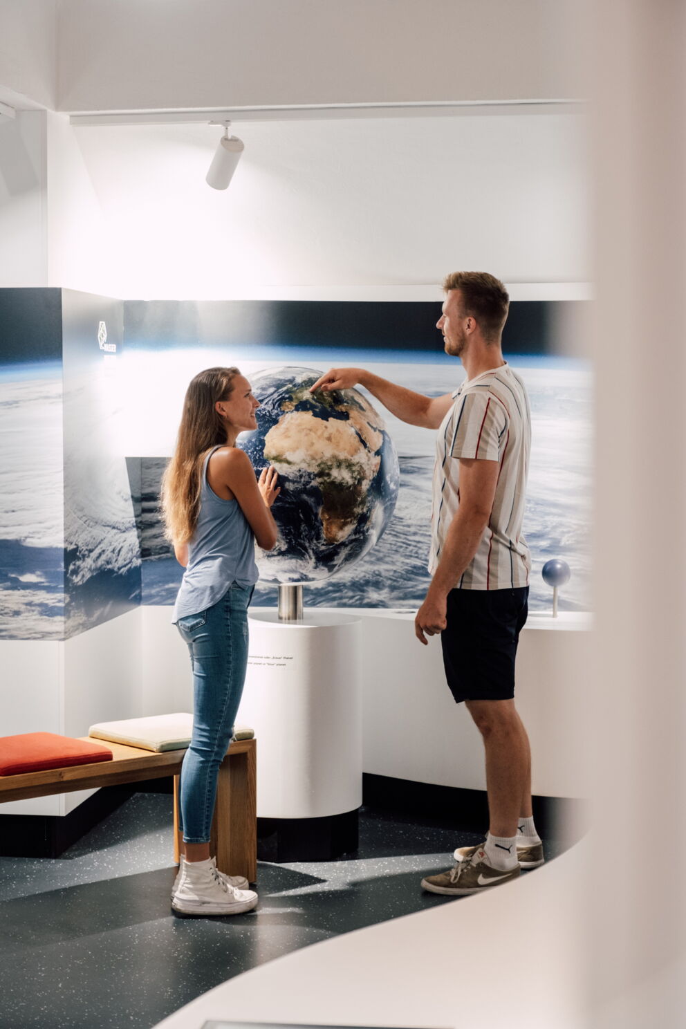 Two people look at a globe together in a modern exhibition room.