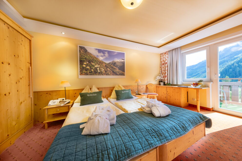 Helles Zimmer mit Holzmöbeln, großer Fensterfront und Ausblick auf die Berge.