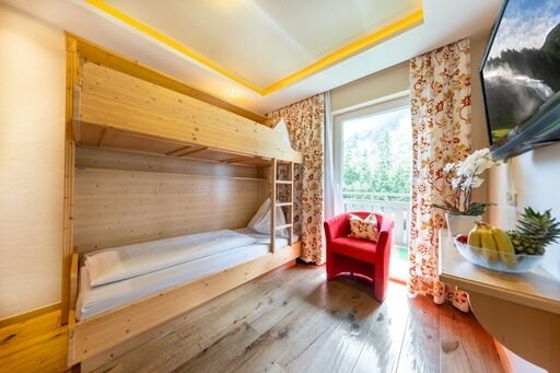 Zimmer mit Etagenbett, Holzverkleidung, rotem Sessel, Balkon und natürlichem Tageslicht.
